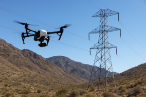 A drone flying alongside a high-voltage transmission line across rugged terrain, capturing data and imagery.